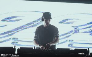Alix Perez alla consolle con proiezioni visive glitch sullo sfondo del palco