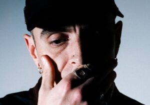 Primo piano di Alix Perez con cappellino e anelli, sguardo rivolto verso il basso