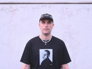 Alix Perez ritratto frontale con cappellino e t-shirt grafica su sfondo neutro