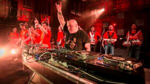 Ice One si esibisce dal vivo con una band di fiati sul palco tra luci rosse