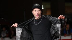 Clementino sorridente sul red carpet con giacca nera e collana, protagonista del rap napoletano in classifica