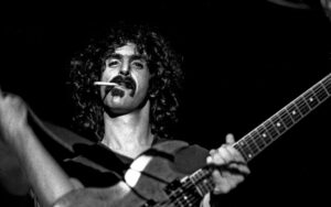 Frank Zappa in bianco e nero con la chitarra e una sigaretta in bocca