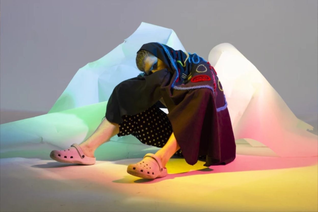 Creatura gelatinosa a forma di verme con un piccolo cappello da strega che fluttua in un wormhole luminoso tra frutta sospesa e nebbia rosa, in stile digitale futuristico