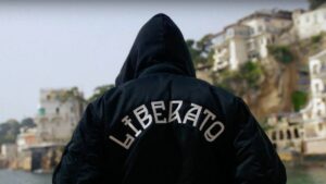 Persona di spalle con felpa nera e scritta LIBERATO, sullo sfondo la costa napoletana