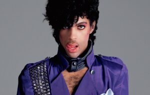 Prince in giacca viola con borchie e trucco, ritratto simbolo dell'era di Purple Rain