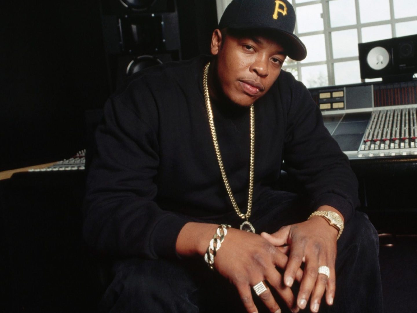Dr. Dre seduto accanto al mixer di uno studio di registrazione, con cappellino e catena d'oro