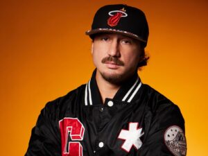 Jangy Leeon, rapper milanese, in un ritratto con cappellino e giacca bomber nera su sfondo arancione