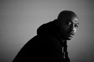 Ka, rapper di Brownsville, in un ritratto in bianco e nero con cappuccio scuro e sguardo rivolto alla camera
