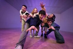 Gruppo di ballerini della crew di Kyle Hanagami che allungano le braccia verso la camera in una sala dalle luci viola