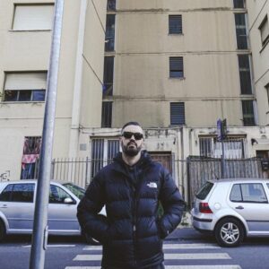Naesh in posa davanti a un palazzo, con occhiali da sole e piumino scuro