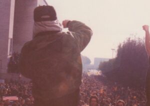 Un rapper di spalle con il pugno alzato davanti alla folla di un corteo studentesco ai tempi della Pantera