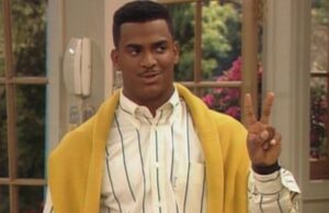 Alfonso Ribeiro nei panni di Carlton Banks con cardigan giallo e segno di vittoria in una scena di Willy, il principe di Bel-Air