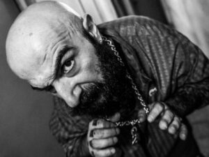 Ritratto in bianco e nero del rapper romano Zinghero che guarda in camera, con catena al collo
